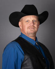 Carl Christian headshot man in a blue shirt, black vest, and black cowboy hat